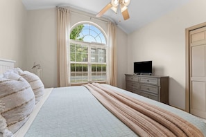 A bedroom with a bed, a television on a dresser, and a window with curtains.