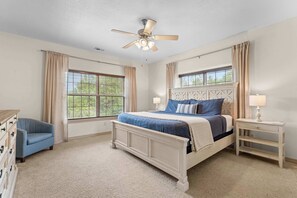 A bedroom with a bed, two bedside tables, a chair, and a ceiling fan.