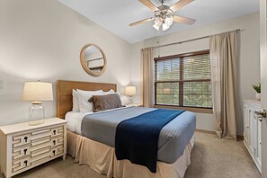 A bedroom with a bed, a nightstand, a dresser, a ceiling fan, a window with blinds, and a radiator.