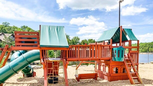 A wooden playground with a slide, swings, and a climbing structure on a sandy beach.