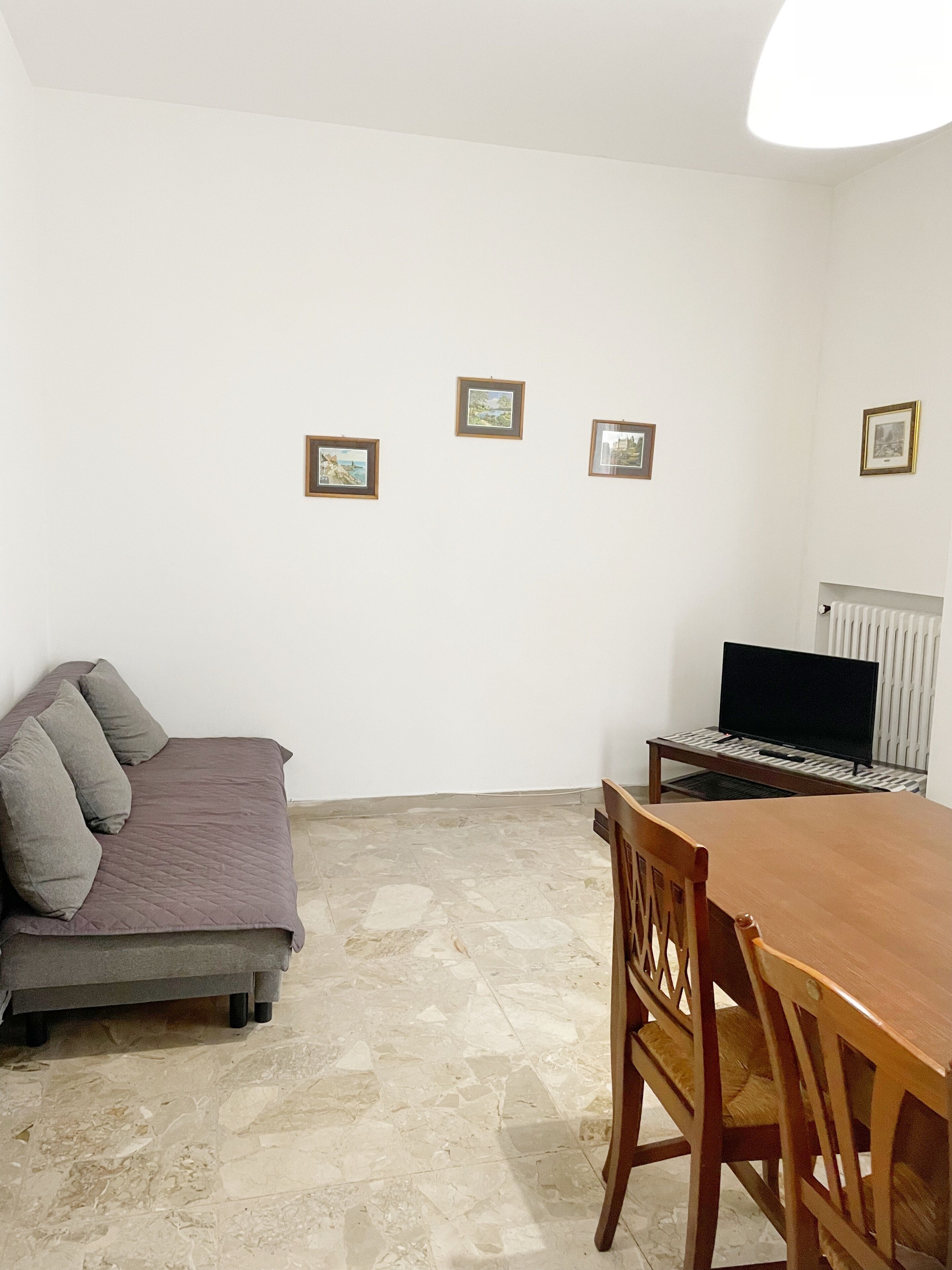 Una habitación con cama, una mesa de comedor y un televisor. Hay tres cuadros en la pared.