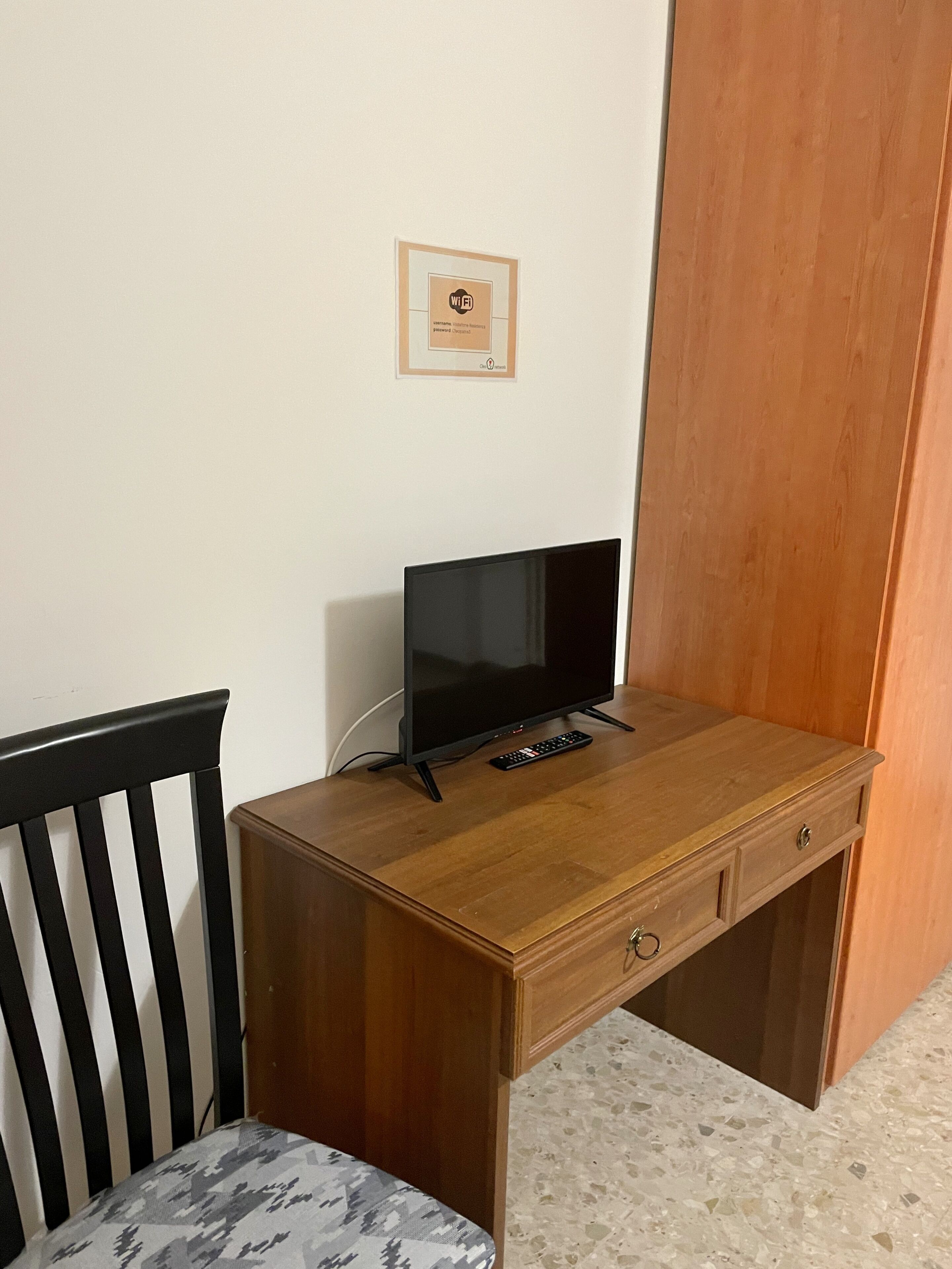 A wooden desk with a television, remote control, and a framed Wi-Fi symbol on the wall.