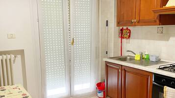 Una cocina con armarios de madera, una estufa y un lavabo. Hay una mesa con mantel y una silla.