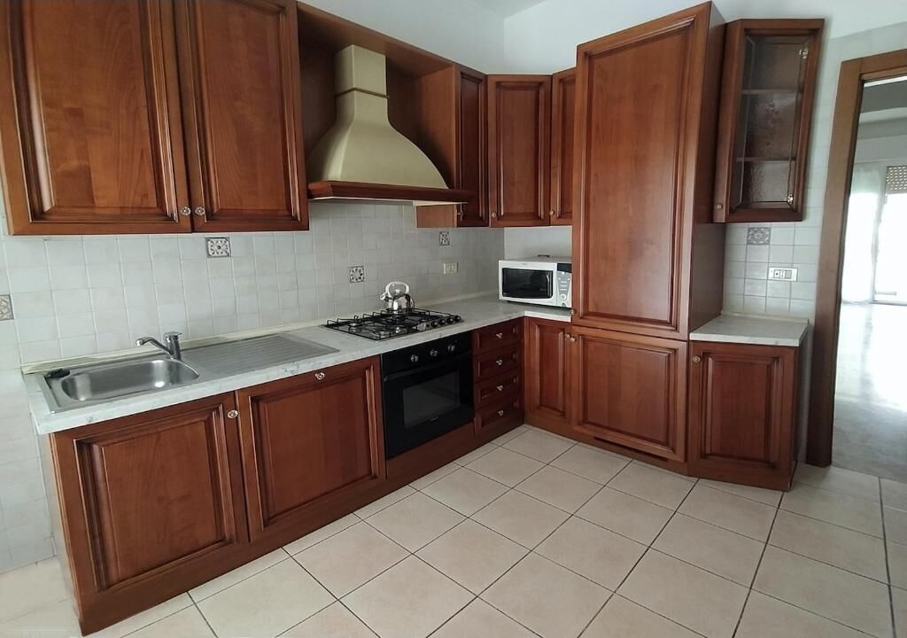 Una cocina con armarios de madera, estufa a gas, microondas y pileta.