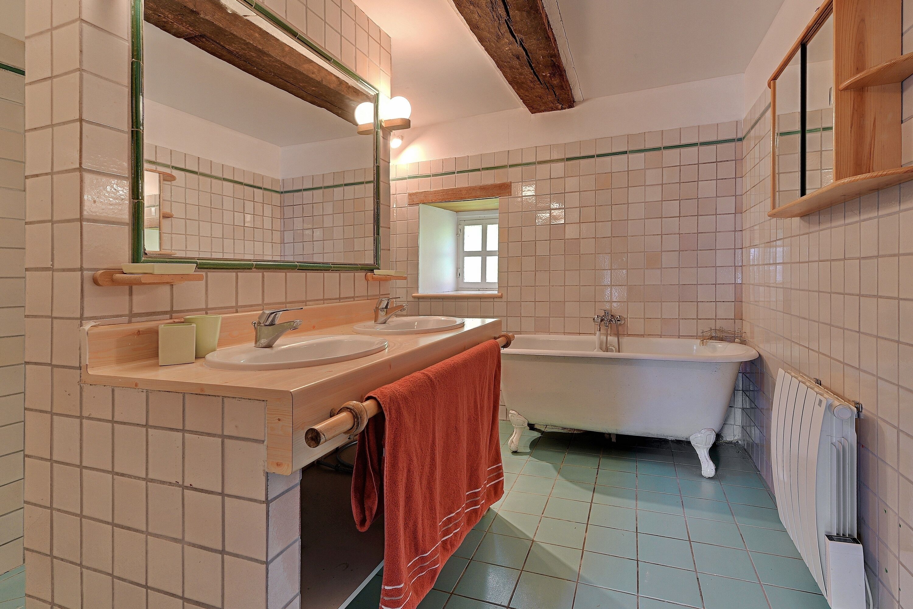 Une salle de bain avec deux lavabos, une baignoire, un miroir et une fenêtre.