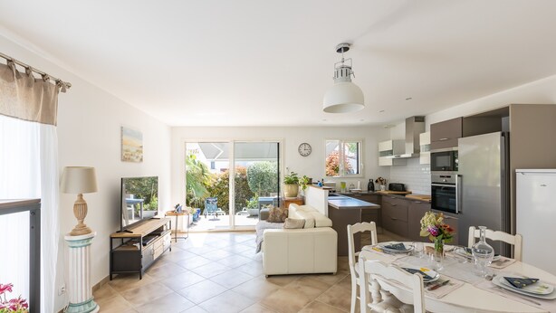 A modern kitchen with a dining area, large windows, and a view of the garden. - Cibelle - Charmante maison avec terrasse (Cers)