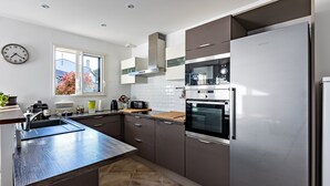 A modern kitchen with stainless steel appliances, a large window, and a built-in oven. - Cibelle - Charmante maison avec terrasse (Cers)