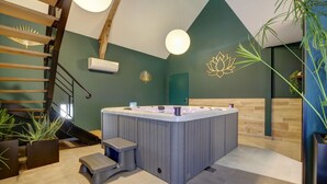 A modern spa area with a hot tub, a staircase, and potted plants. - Un nid dans la Grange - Maison avec jacuzzi et sauna (Boué)