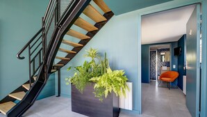 A modern interior with a black staircase, a large planter with green plants, and a bright orange chair. - Un nid dans la Grange - Maison avec jacuzzi et sauna (Boué)