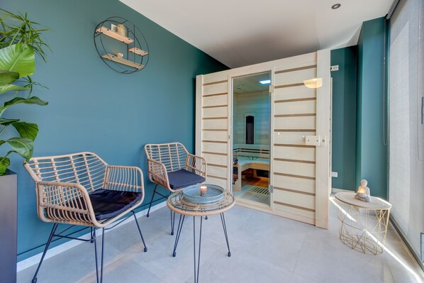 A modern room with teal walls, two wicker chairs, a small round table with a candle, and a view into an adjacent room through a sliding door.