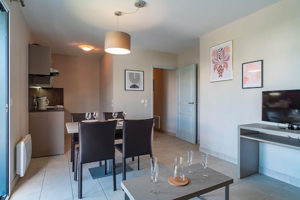 Enjoy meals together at the dining table for two, accompanied by a mounted TV and kitchen area.