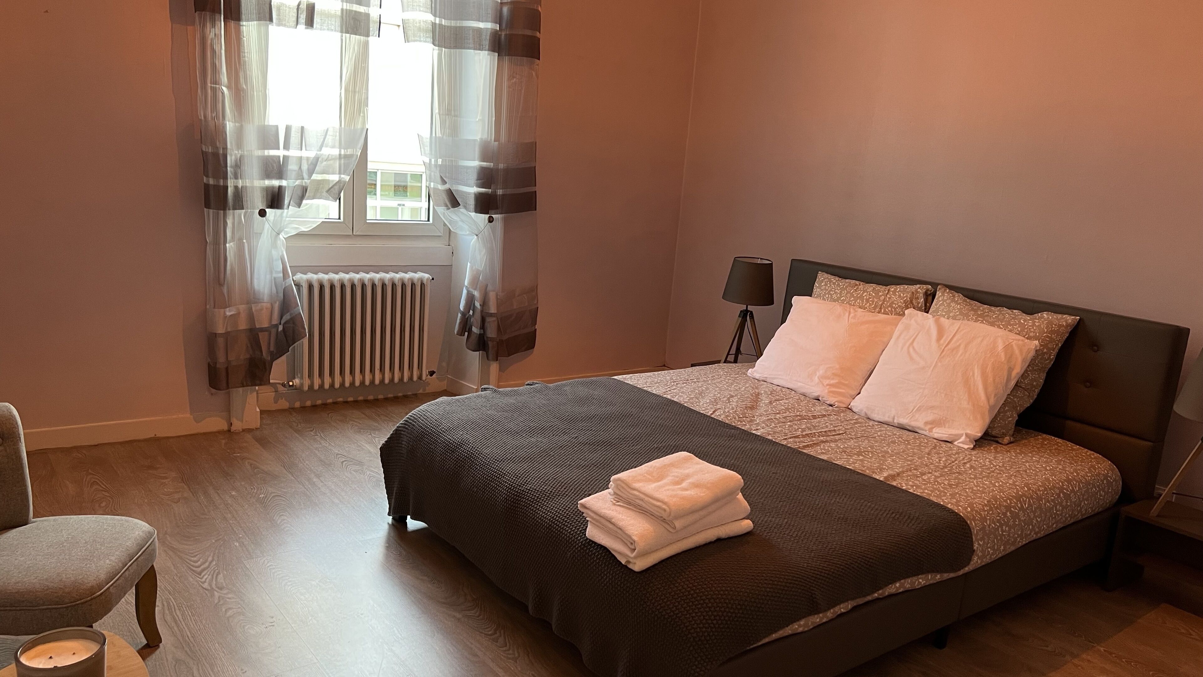 A bedroom with a bed, a chair, a radiator, and a lamp.