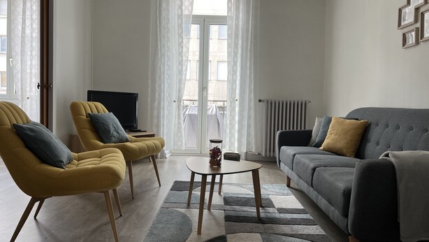 Un salon avec deux fauteuils jaunes, un canapé gris, une petite table basse et un téléviseur posé sur un meuble.