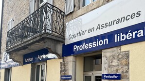 Un immeuble où plusieurs enseignes indiquent différents métiers et services, notamment « Artisan Agriculteur » et « Courtier en Assurances ».