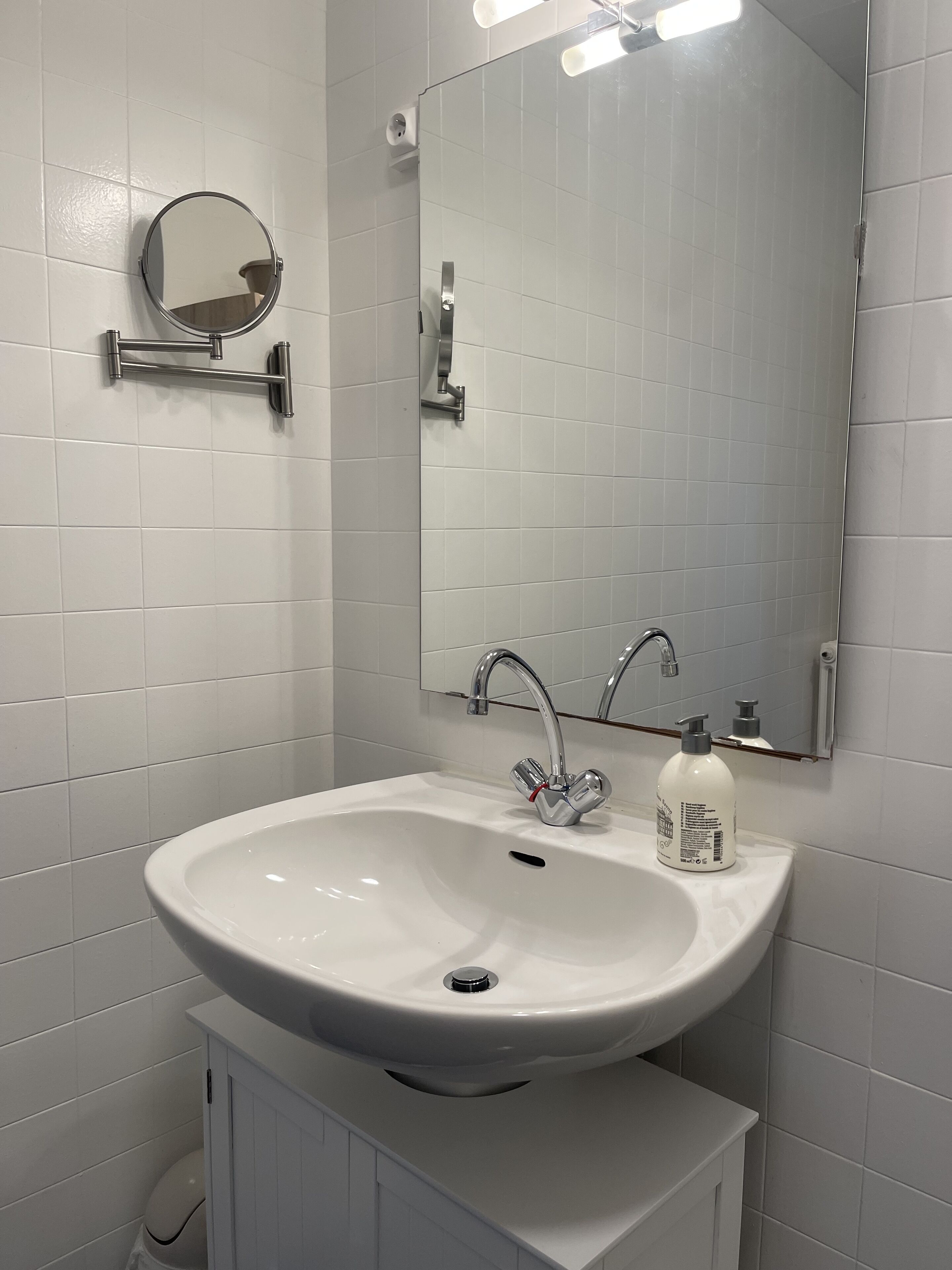A bathroom with a white sink, a mirror, and a bottle of hand soap.