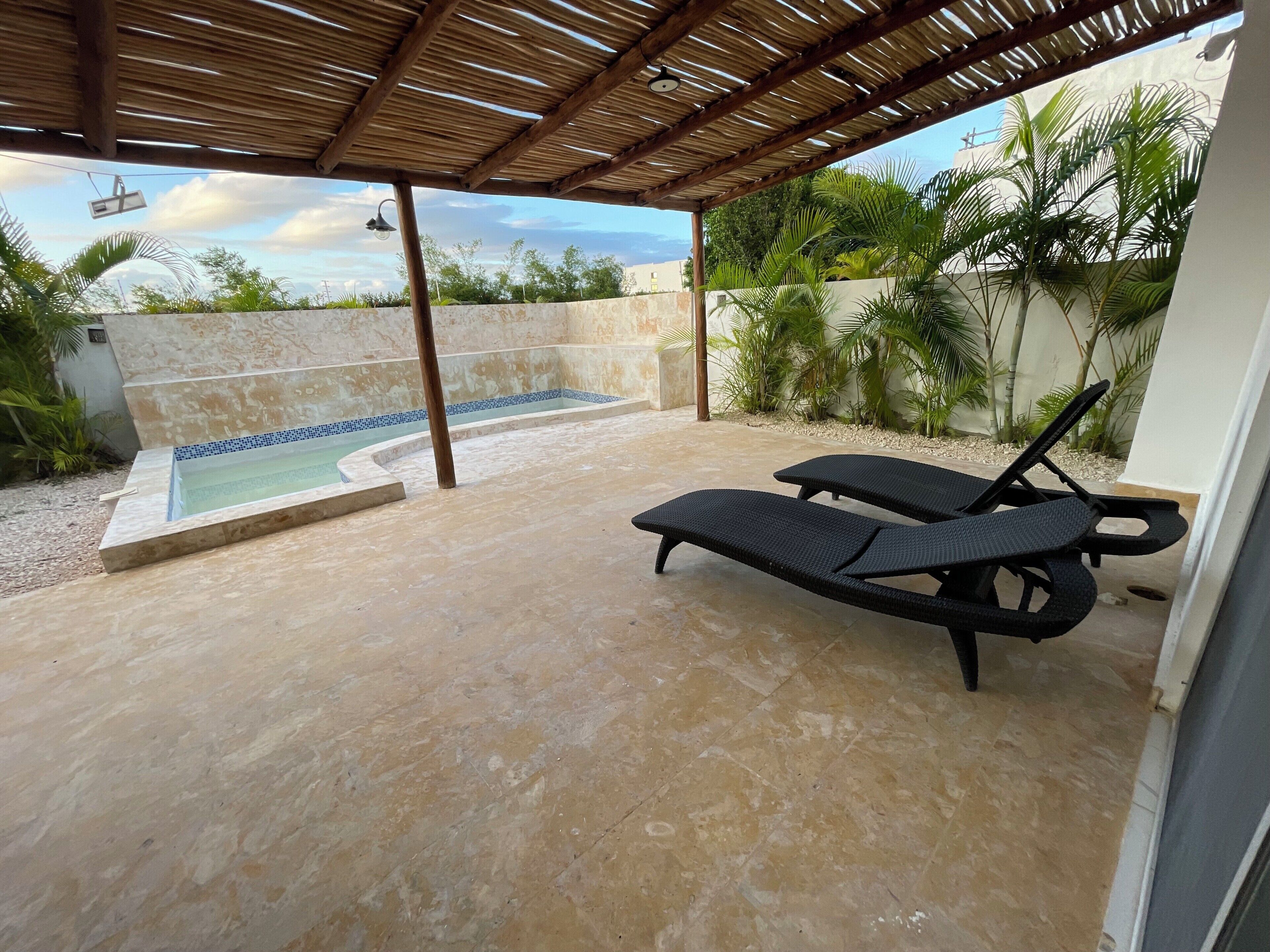 Ein überdachter Außenbereich mit Pool, Liegestühlen und einer Pergola.