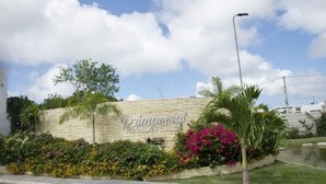Een bordje voor Primaveral Residences, met een stenen muur, kleurrijke bloemen en een palmboom.