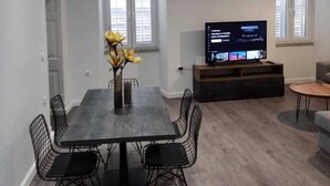 A modern living room with a dining area, a flat-screen TV, and a vase with yellow flowers. - Saint's View Apartments (Corfu)