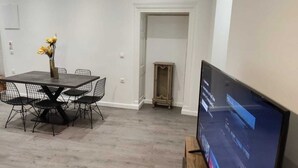 A dining area with a table and chairs, a television on a stand, and a door leading to another room. - Saint's View Apartments (Corfu)