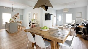 A spacious living area with a wooden dining table, white chairs, and a modern pendant light. - Scandi Candi (Atlanta)