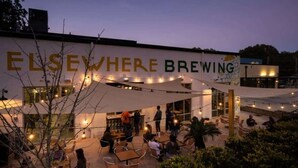 An outdoor seating area of a restaurant named 'ELSEWHERE BREWING' with tables and chairs under a canopy. - Scandi Candi (Atlanta)