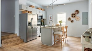 A modern kitchen with a central island, stainless steel appliances, and a wooden staircase leading to another room. - Scandi Candi (Atlanta)