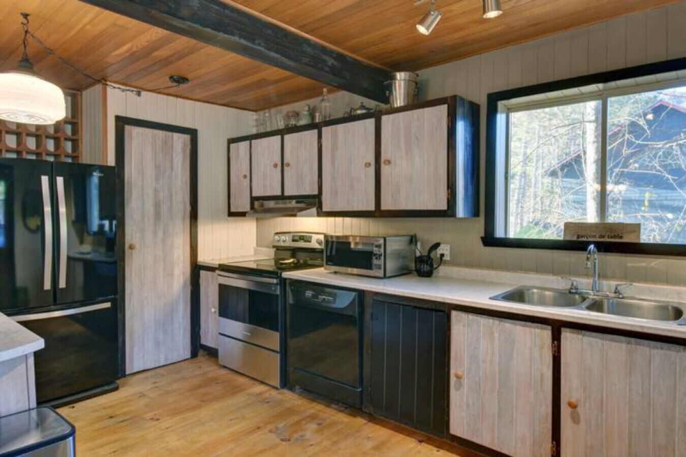 A modern kitchen with wooden cabinets, stainless steel appliances, and a large window providing a view of the outdoors.