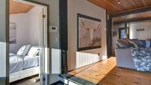 A room with a bed, a large wall-mounted artwork of a cow skull, a wooden ceiling, and a sofa with a fur throw.