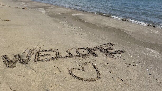 Een strand met 'WELCOME' en een hart getekend in het zand.