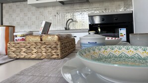 Een keuken met witte kasten, een betegelde spatwand, een Nuella pot, een broodmand, een Buondi verpakking en een decoratieve kom.
