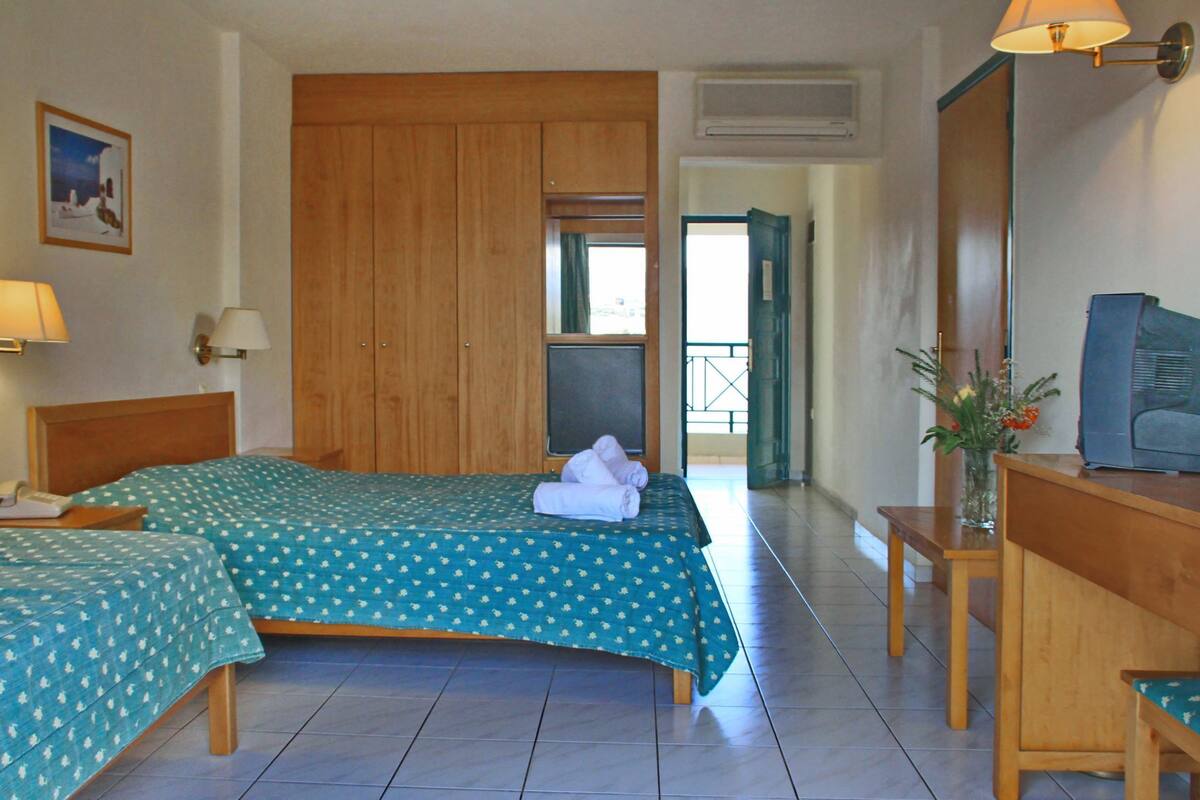 Habitación de hotel con dos camas, un escritorio, una silla, una lámpara, un televisor y una ventana con vistas.