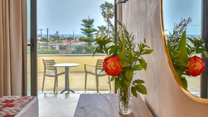 Un dormitorio con cama de madera, una mesita de noche con un florero, un espejo grande y vistas al balcón con sillas y una mesa.