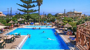 Una piscina con sillas de descanso y sombrillas, rodeada de vegetación y edificios.