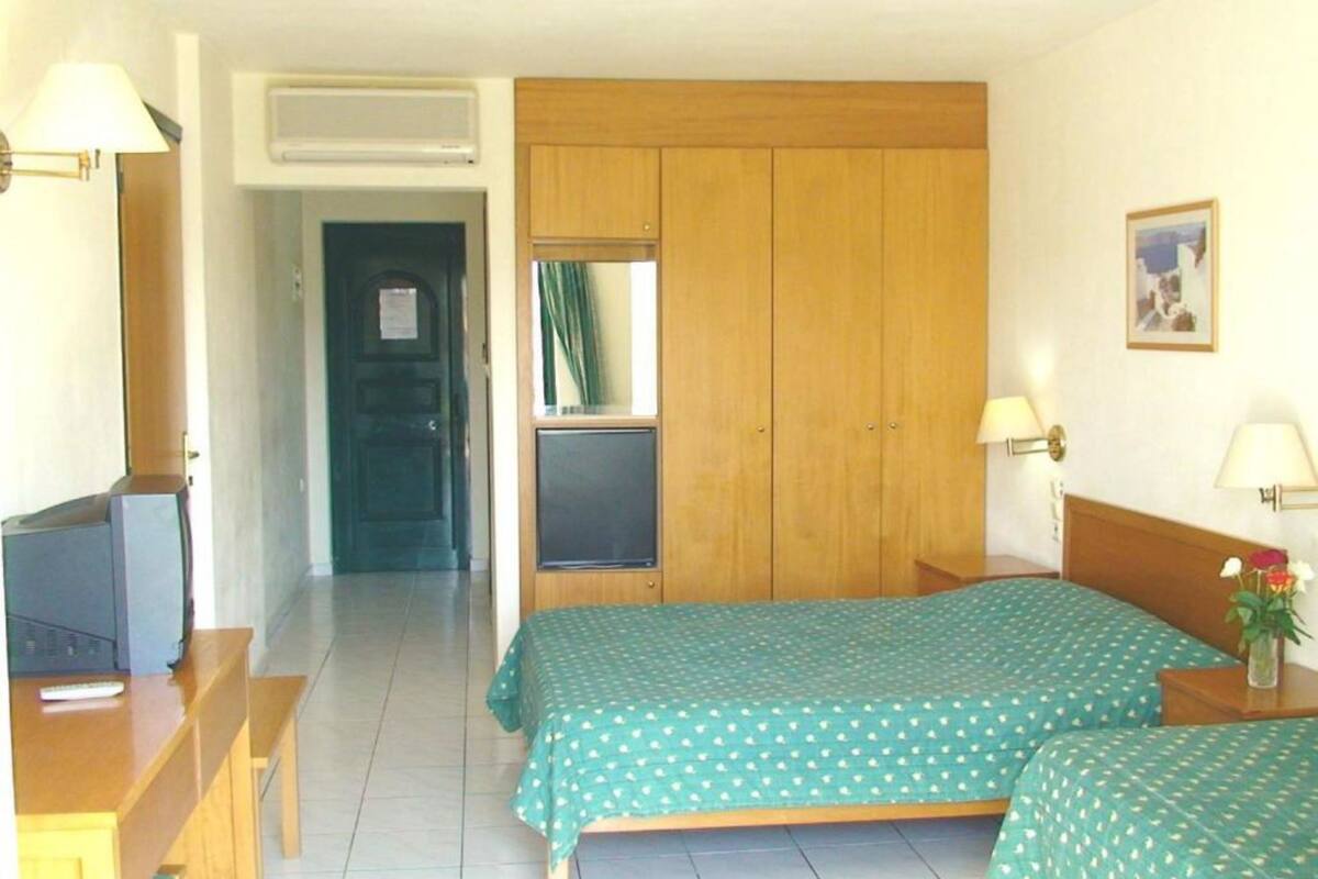 Habitación de hotel con dos camas individuales, un escritorio con silla, televisor y armario.