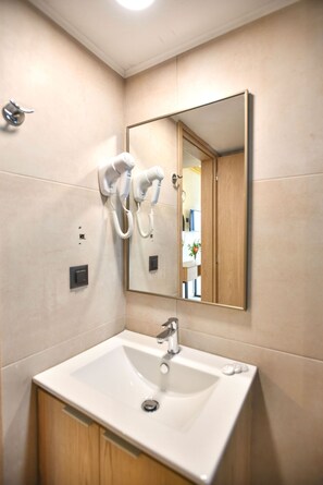 A bathroom with a white sink, a mirror, and a hairdryer mounted on the wall. - Despo Hotel by Estia (Hersonissos)