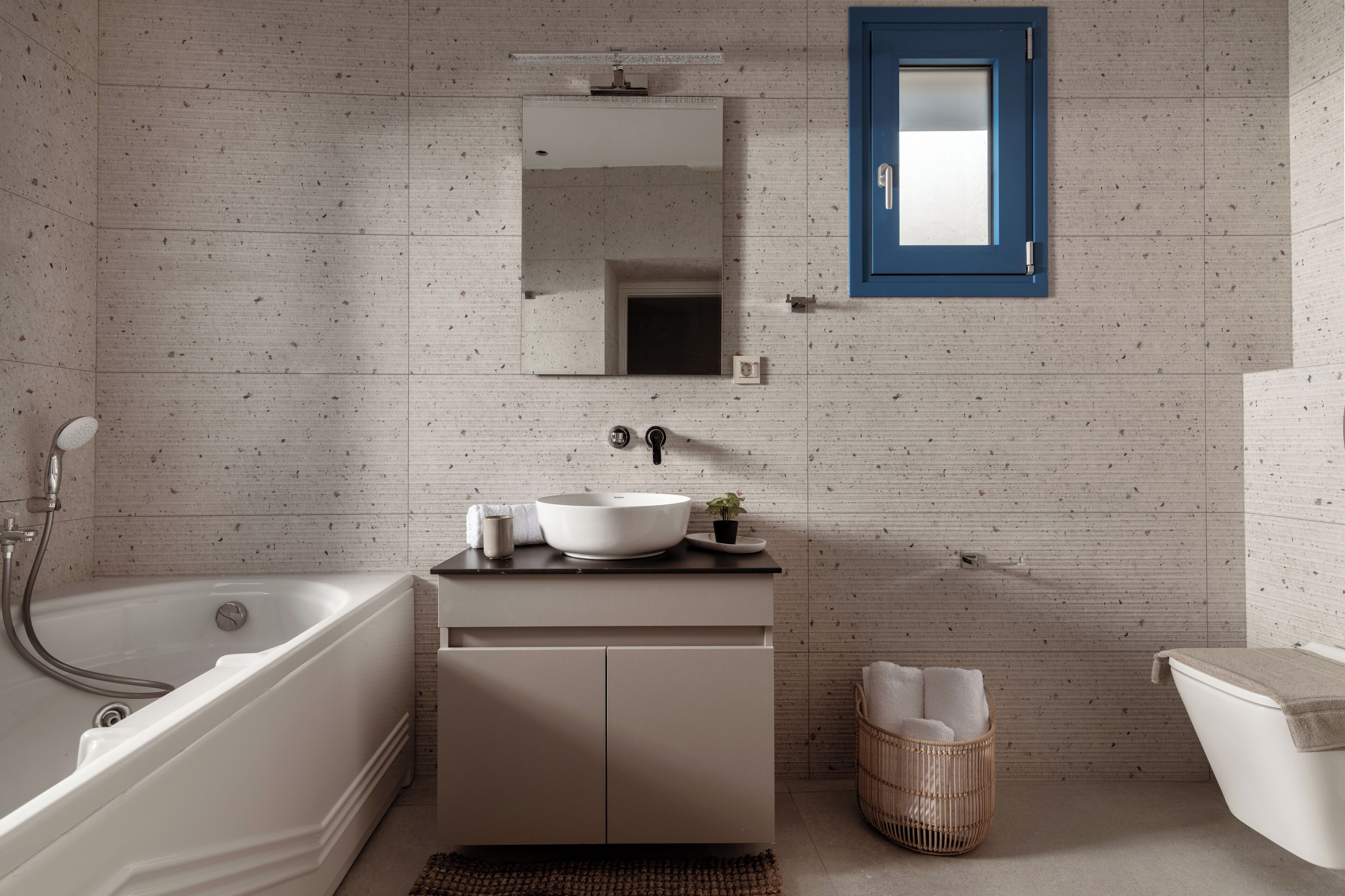 Une salle de bain moderne avec une baignoire sur pieds, un lavabo blanc avec un receveur, une petite plante en pot et un panier en osier.