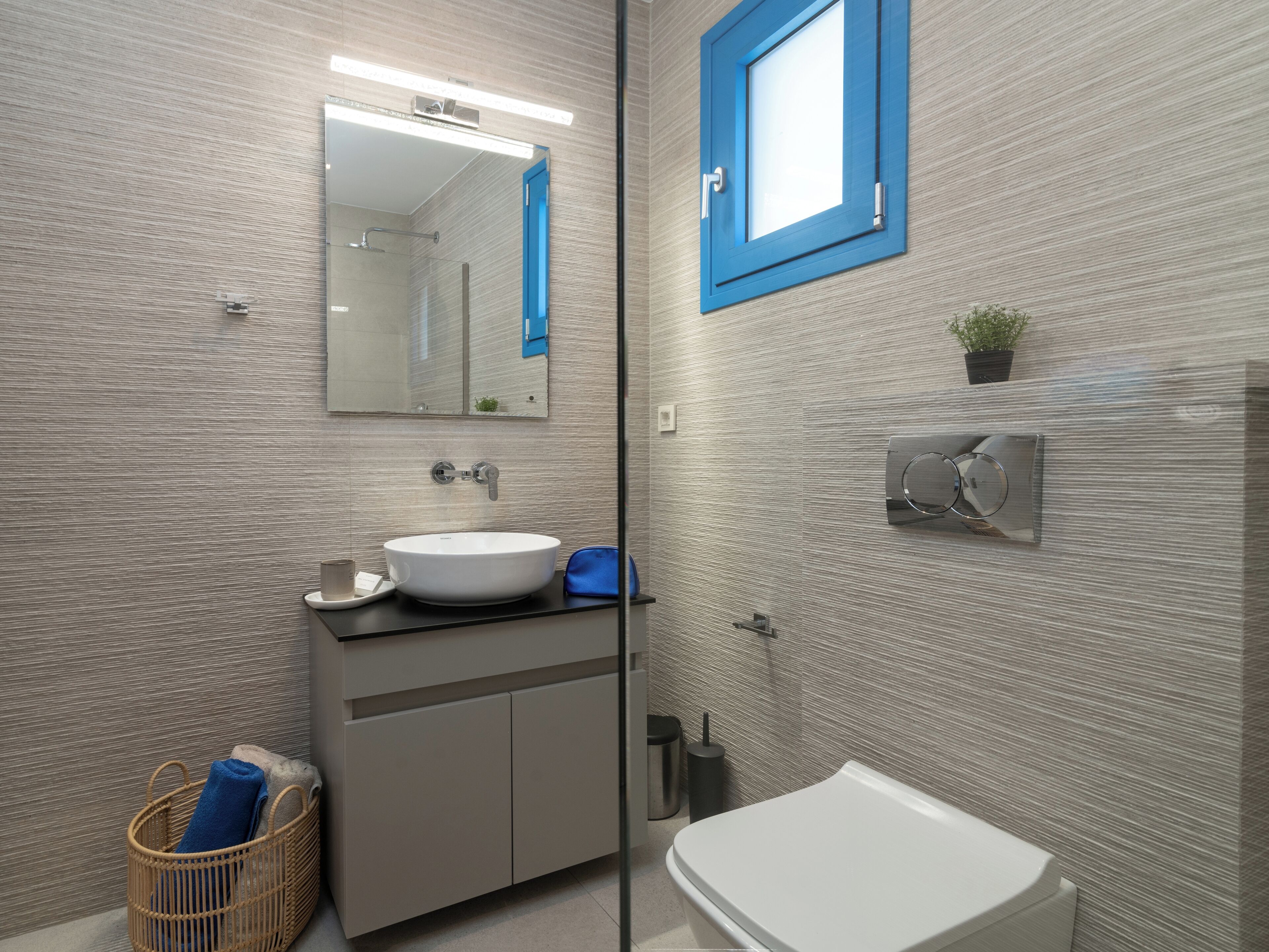 Un baño moderno con un espejo grande, un lavamanos blanco, un inodoro y una pequeña planta en maceta.