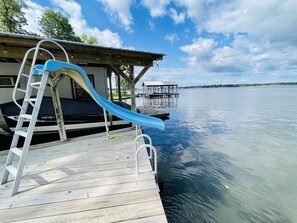 Enjoy a serene lakeside retreat with a dock offering a blue slide and shaded relaxation area.