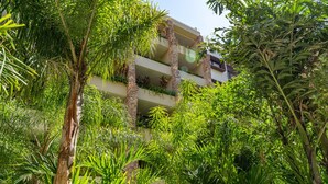 Un immeuble à plusieurs étages doté de balcons, entouré d’une végétation tropicale luxuriante.