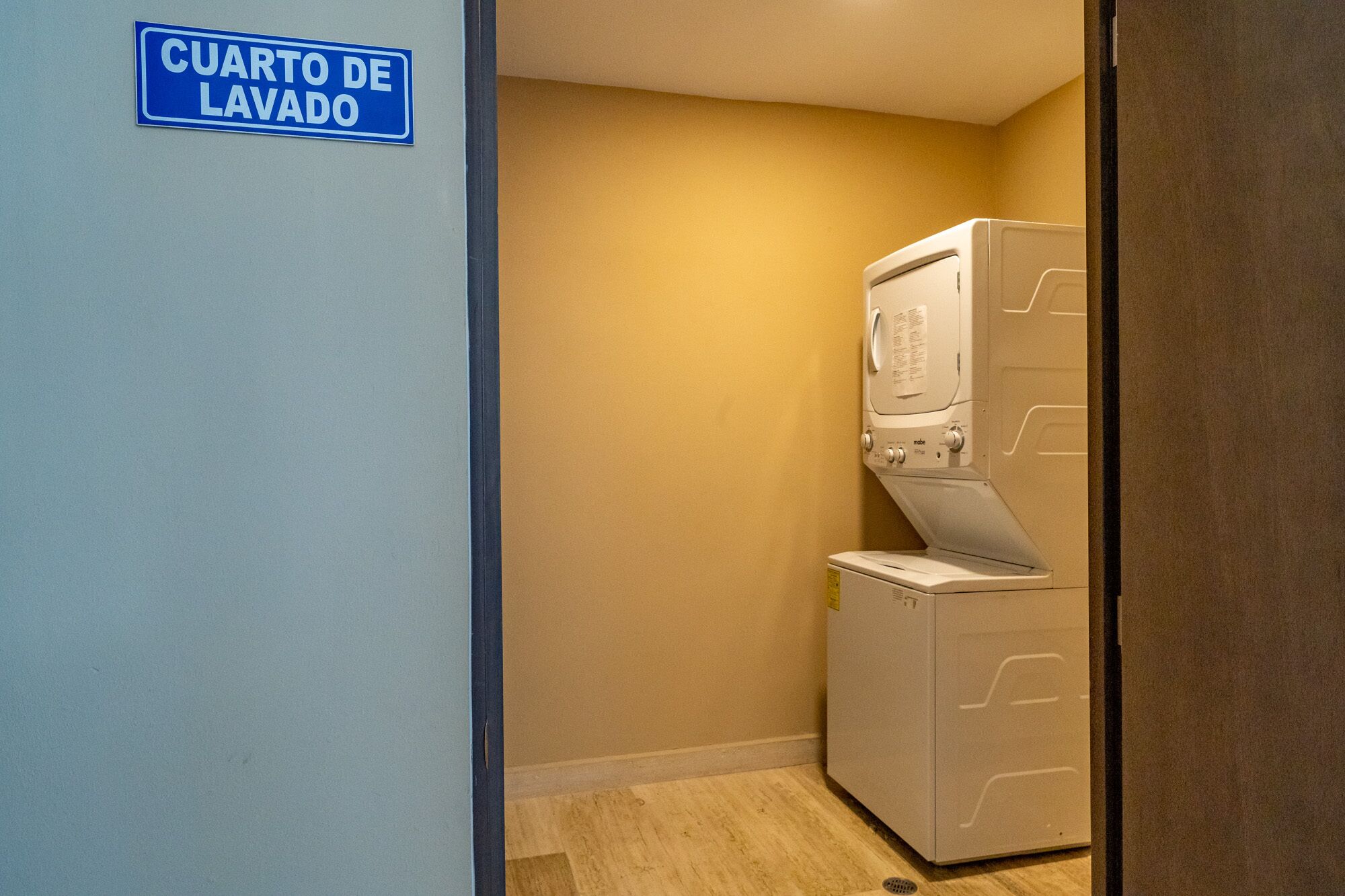 Ein Waschraum mit einem Schild, auf dem 'CUARTO DE LAVADO' steht, und einer gestapelten Waschmaschine und einem Trockner.