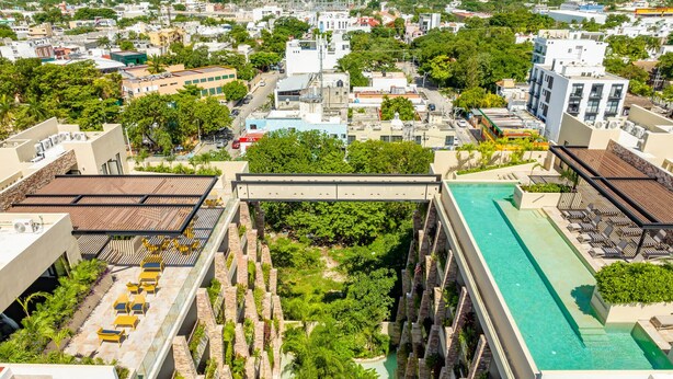 Un hôtel de grande hauteur doté d’une piscine sur le toit, d’une végétation luxuriante et offrant une vue sur le paysage urbain.
