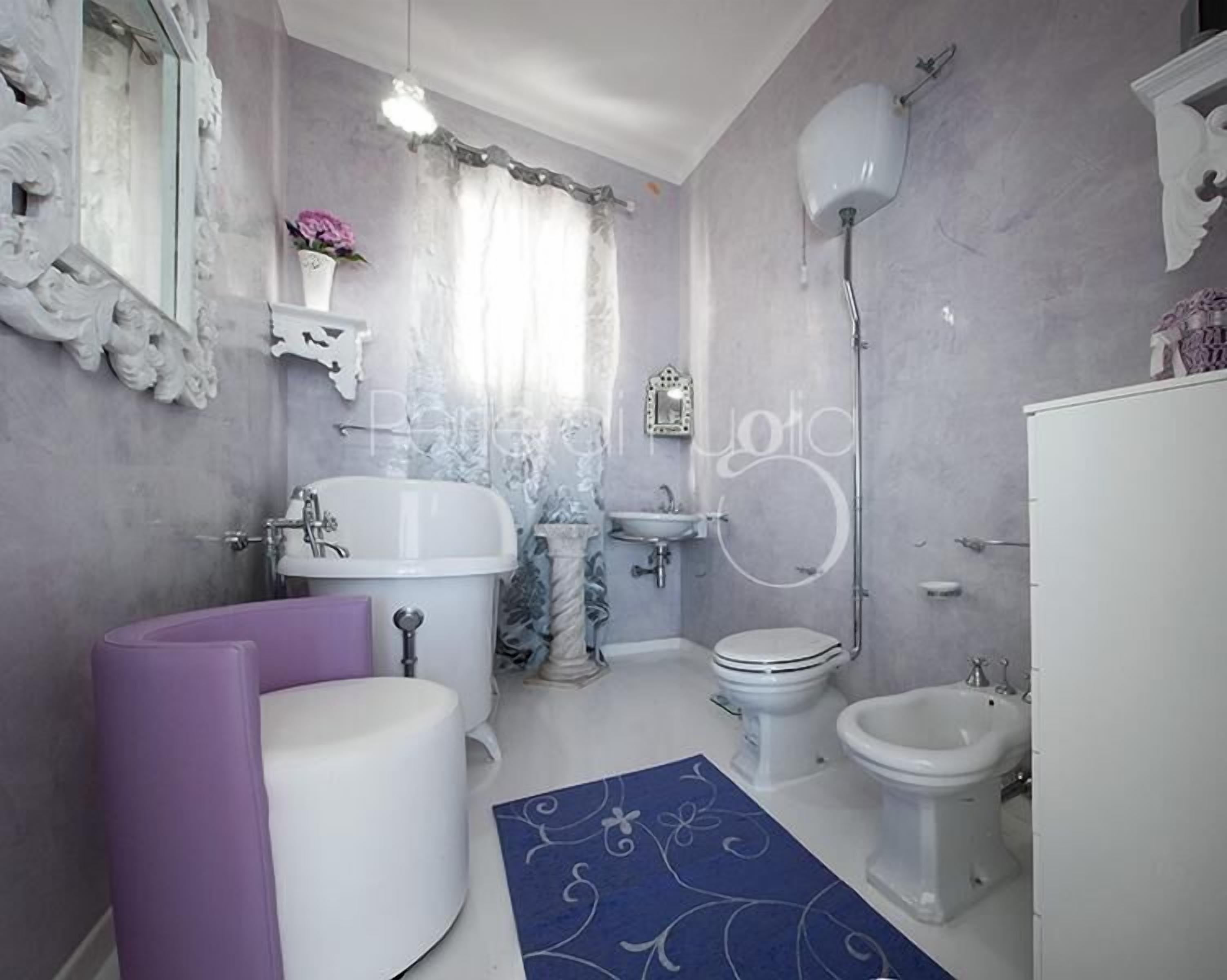 A bathroom with a bathtub, sink, toilet, bidet, and decorative elements like a mirror and wall art.