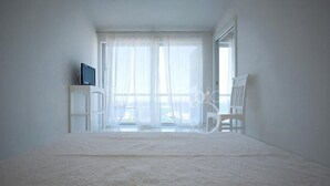 A room with a bed, a chair, a television on a stand, and a window with sheer curtains. - 3361 Attico Barca by Barbarhouse (Gallipoli)