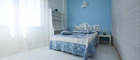 A bedroom with a bed, a nightstand, a wall-mounted decoration, and a window with sheer curtains.