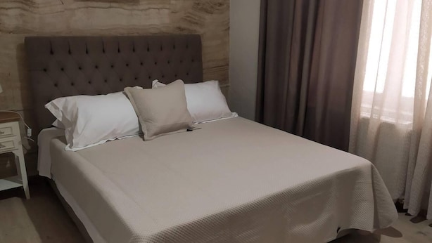 A neatly made bed with a tufted headboard, a bedside table, and a window with curtains.