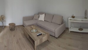 A minimalist living room with a light-colored sofa, a wooden coffee table, and a white side table with decorative items.