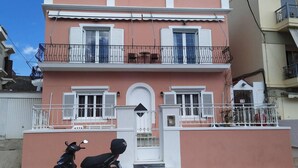 A two-story building with a pink facade, white shutters, and a balcony with metal railings.