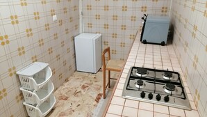 Uma cozinha compacta com fogão a gás, geladeira e uma cadeira.