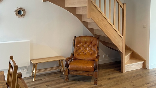 A spacious room with a wooden staircase, a leather armchair, a wooden bench, and a dining table with chairs. - Maison de campagne, Sainte Mère Église, site historique (Sainte-Mère-Eglise)
