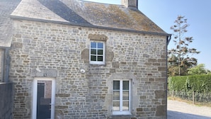 A stone building with a white door, two windows, and a small porch area. - Maison de campagne, Sainte Mère Église, site historique (Sainte-Mère-Eglise)